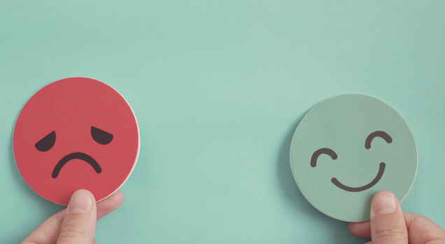 Mãos segurando expressões de tristeza e alegria.