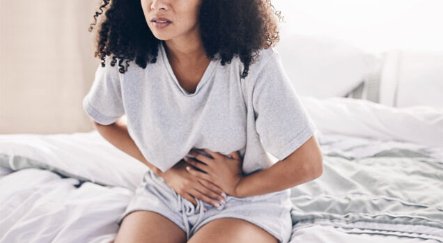 Mulher com dor abdominal sentada na cama
